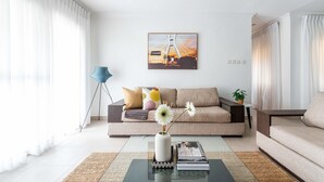 Een moderne woonkamer met een bank, een bijzettafeltje met een vaas en boeken, en een schilderij aan de muur.