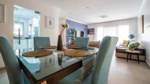 Een moderne woonkamer met een glazen eettafel, blauwgroene stoelen en een bank met bijzettafeltje.