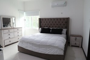 A bedroom with a large bed, a dresser, a nightstand, and a mirror. - Quiet , pool, gated,security (kingston 19)