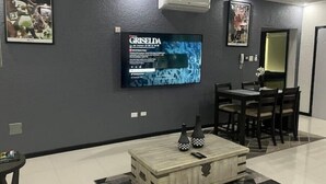 A modern living room with a flat-screen TV mounted on the wall, a wooden coffee table, and a dining area with a table and chairs. - Quiet , pool, gated,security (kingston 19)