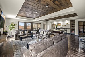 A spacious living room with leather sofas, a coffee table, and a fireplace. There is a dining area with a table and chairs, and a kitchen in the background.