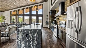 Une cuisine spacieuse dotée d’un grand îlot central, d’appareils électroménagers en acier inoxydable et d’un plafond en bois.