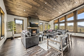 A spacious living room with a fireplace, large windows, and a high ceiling.
