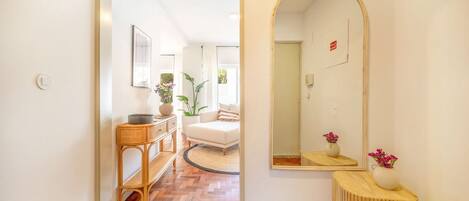 A hallway with a wooden herringbone floor, a white sofa, a round rug, and a mirror with a wooden frame.