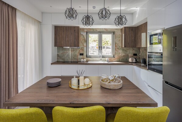 A modern kitchen with a wooden dining table, a built-in oven, and a large window.