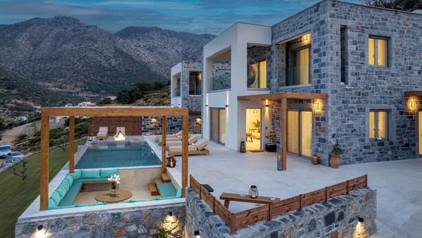 Una casa moderna con piscina, fachada de piedra y vistas a las montañas.