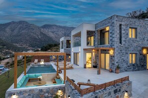 Una casa moderna con piscina, fachada de piedra y vistas a las montañas.
