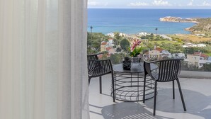 Un balcón con mesa y sillas, con vistas a la costa, casas y el mar.