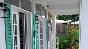 A covered outdoor area with tiled flooring, potted plants, and a seating area with a table and chairs. - Rainbow Inn (St. Andrew)