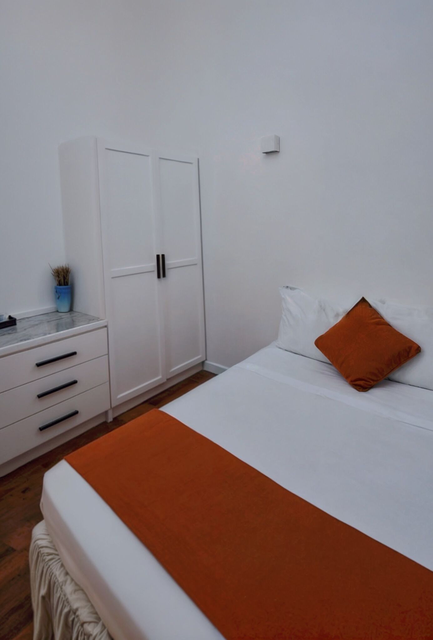 Un dormitorio con cama, armario blanco y una mesita con una planta.