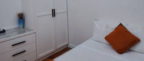 Un dormitorio con cama, armario blanco y una mesita con una planta.