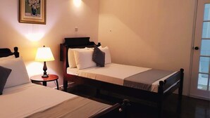 A hotel room with two single beds, a nightstand with a lamp, a framed picture on the wall, and a door leading to a balcony. - Rainbow Inn (St. Andrew)