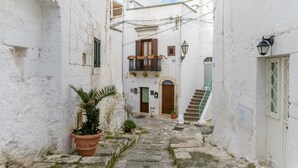 A narrow street with white buildings, a wooden door, and a staircase. - Terrazza Aragonese by Wonderful Italy (Ostuni)