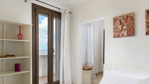 A bedroom with a bed, a nightstand, a window with curtains, a shelf with decorative items, and a painting on the wall. - Terrazza Aragonese by Wonderful Italy (Ostuni)