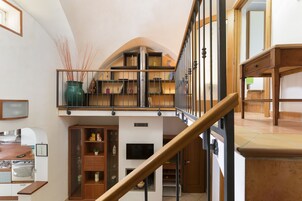 A spacious living area with a high ceiling, a wooden staircase, and a built-in bookshelf.