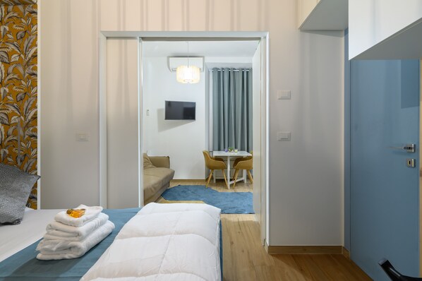 A hotel room with a bed, a desk, a chair, a TV, and a bathroom visible through an open door.