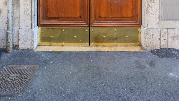 A large wooden double door with brass handles and decorative glass panels, set in a stone wall. - Visconti apartment (Roma)