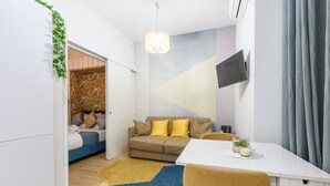A modern, well-lit room with a bed, a sofa, a dining table, and a TV mounted on the wall. - Visconti apartment (Roma)
