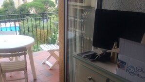 A balcony with a table and chairs, a glass cabinet, and a view of a swimming pool and greenery.