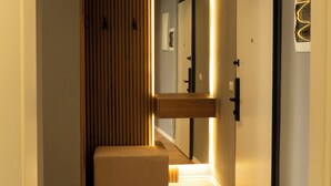 Un couloir doté d’un plancher en bois, d’un banc, d’un miroir fixé au mur et d’une porte.