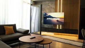 Un salon moderne avec un canapé, une table basse et un téléviseur fixé à un mur texturé où l’on peut voir l’inscription « AFRO HOUSE ».