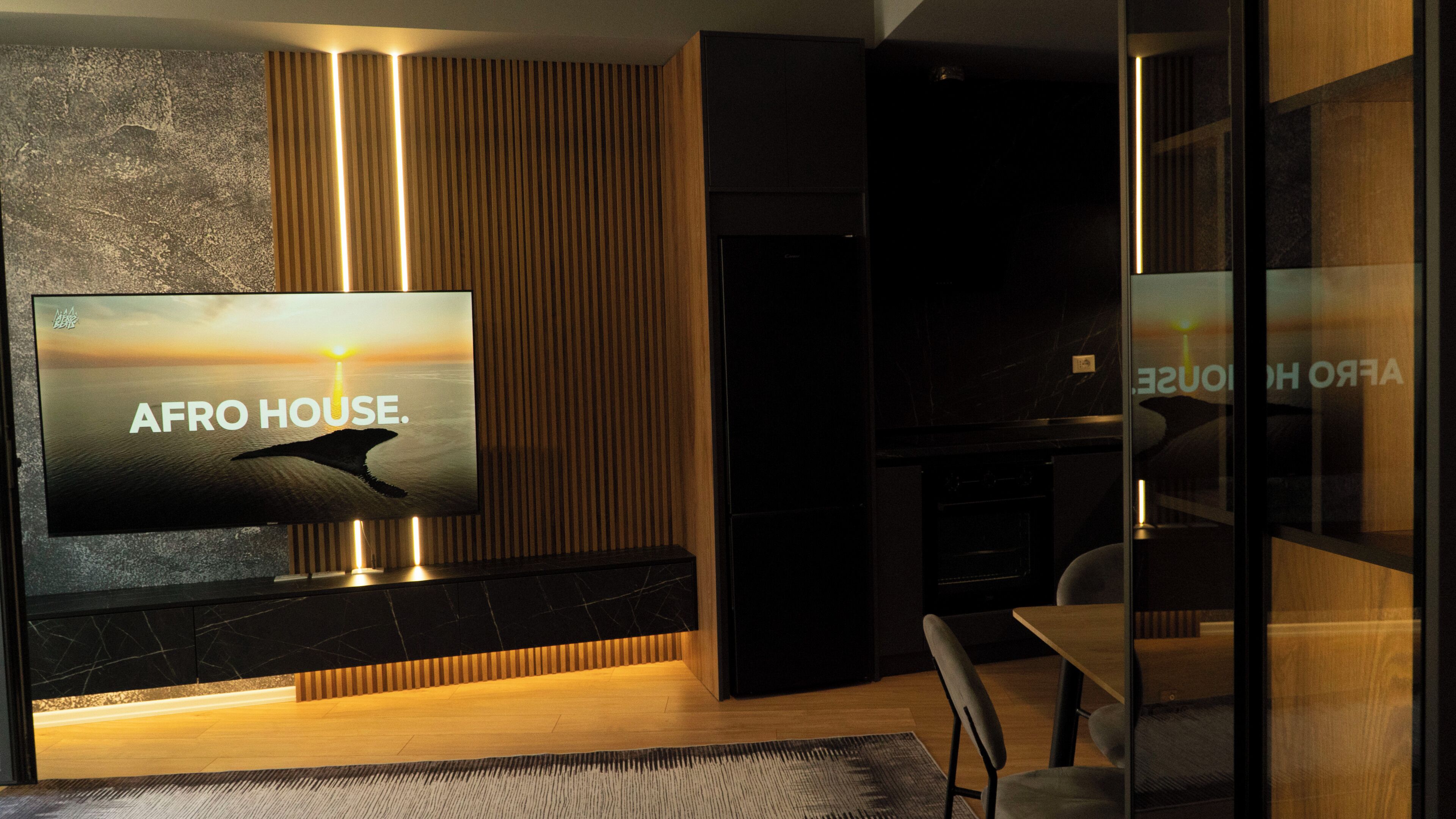 A modern living room with a large flat-screen TV displaying 'AFRO HOUSE.' A wooden panel wall and a dark fireplace are visible.
