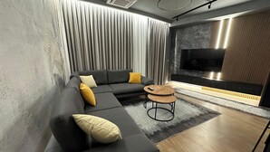 Un salon moderne avec un canapé d’angle, une table basse et un téléviseur à écran plat, le tout placé devant un mur en pierre.
