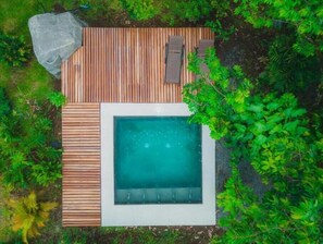 Vista aérea de un jacuzzi rodeado por una terraza de madera, con abundante vegetación a los lados.