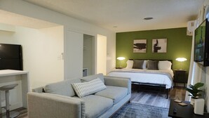 Een moderne hotelkamer met een grijze bank, een bed met witte beddengoed, een bureau met een flatscreen televisie en groene wanden.