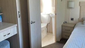 A compact bedroom with a single bed, a bedside table, a desk, and a wardrobe. - Inviting 2-bed Caravan on Combe Haven Holiday Park (St Leonards-On-Sea)
