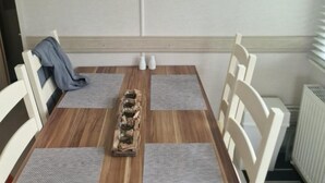 A dining table with four chairs, a wooden centerpiece, a wall clock, and a heart-shaped decoration. - Inviting 2-bed Caravan on Combe Haven Holiday Park (St Leonards-On-Sea)