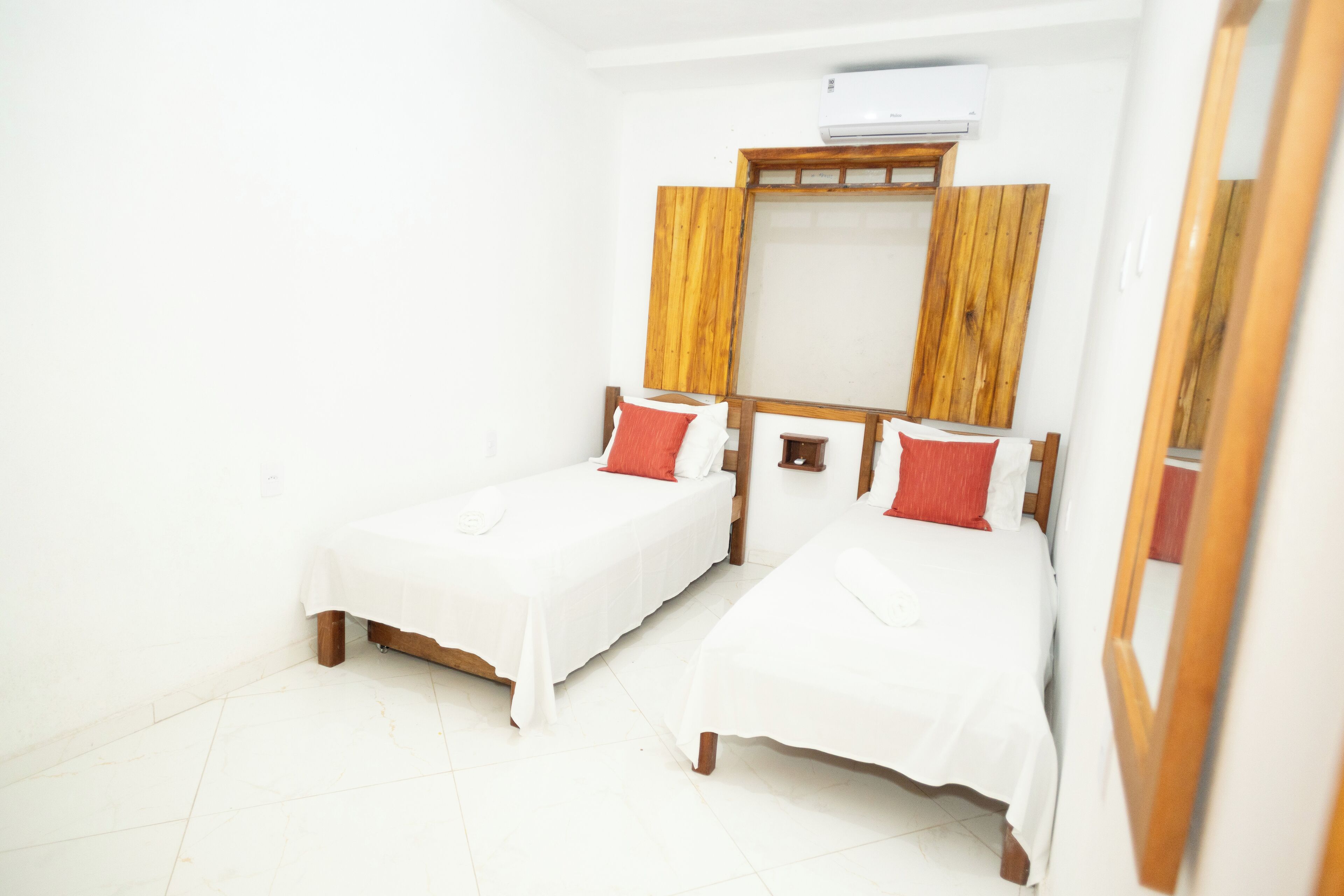 Una habitación con dos camas individuales, ropa de cama blanca, cabeceros de madera y un espejo grande.