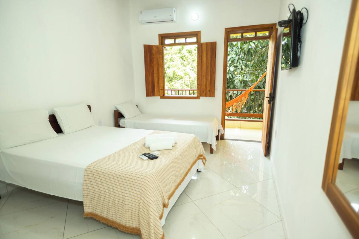 A bedroom with a large bed, a smaller bed, a window with wooden shutters, and a view of a staircase leading outside.