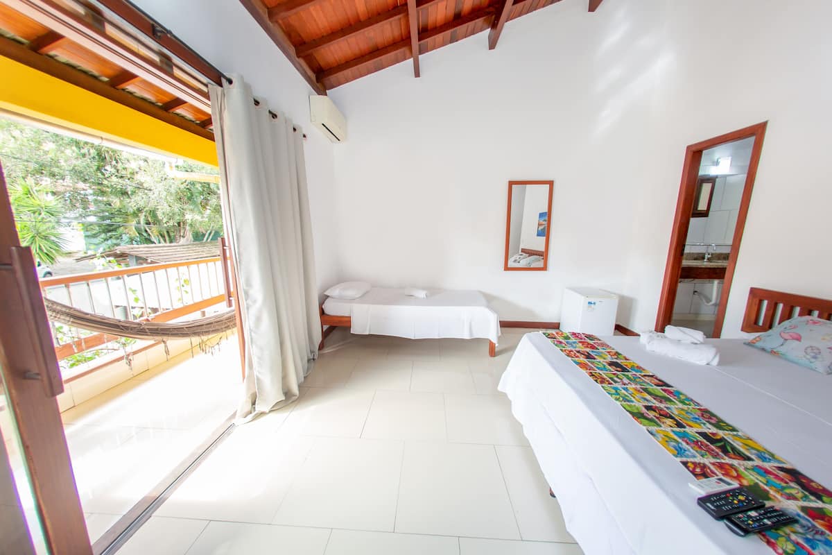A hotel room with a balcony, a bed with a colorful blanket, a bedside table, a mirror, and a window with curtains.
