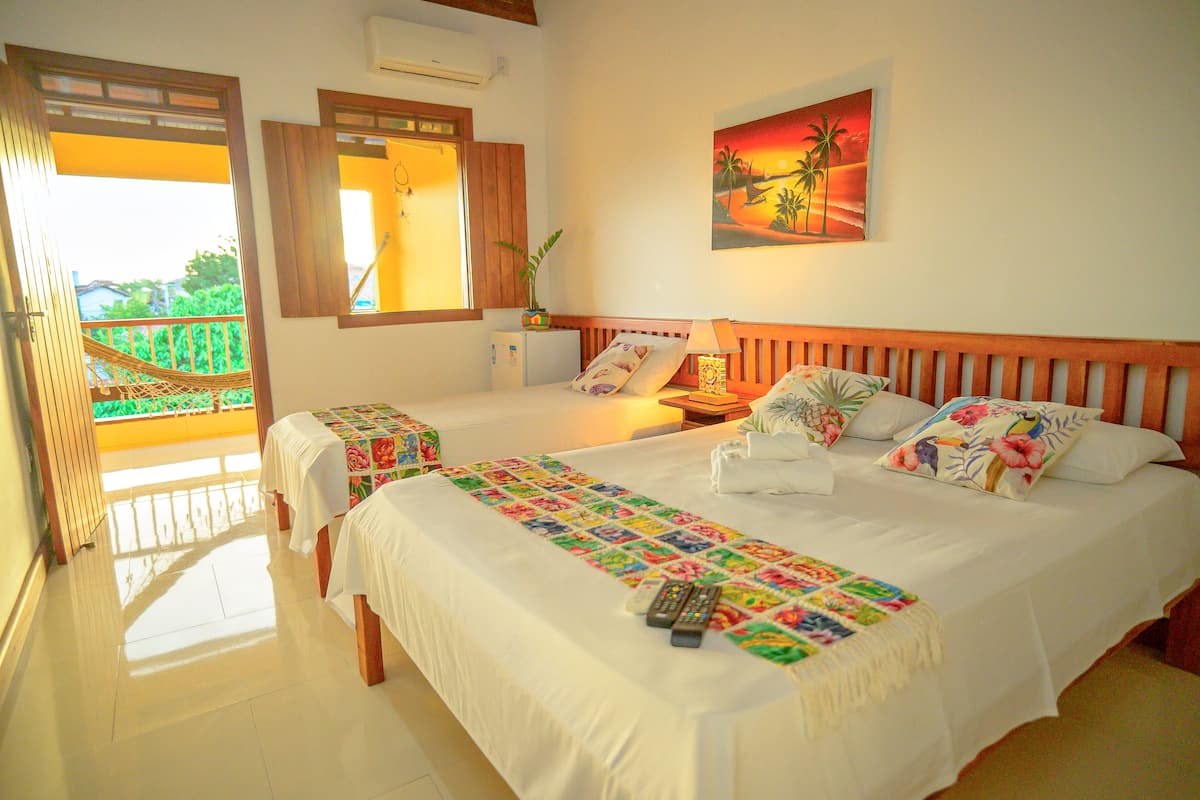 A hotel room with a large bed, a small table, a nightstand, a window with a view, and a painting on the wall.