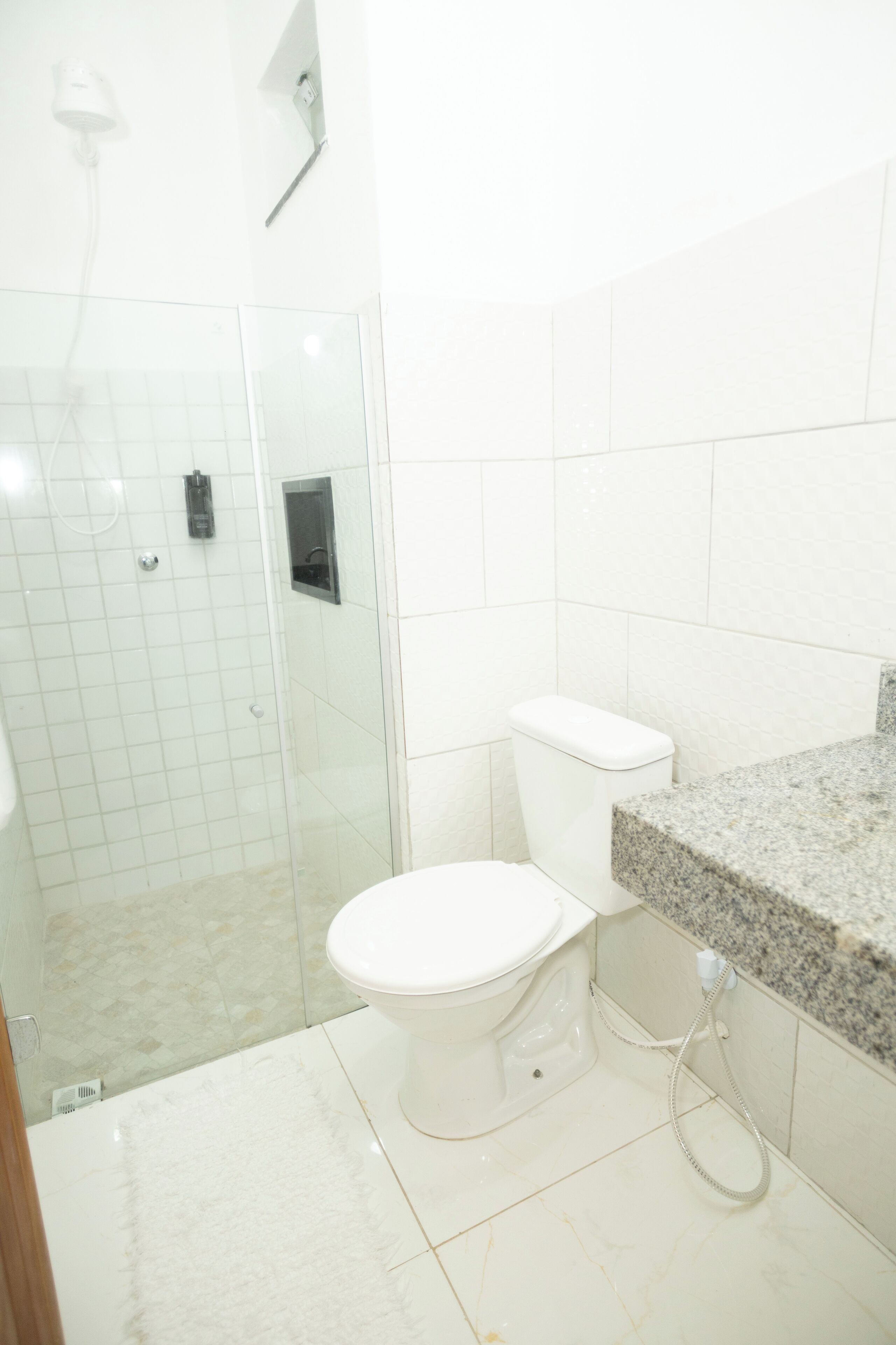 Een badkamer met een douchecabine van glas, een wit toilet en een granieten aanrechtblad.