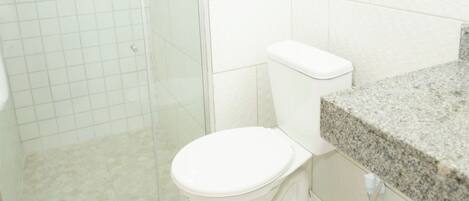 Een badkamer met een douchecabine van glas, een wit toilet en een granieten aanrechtblad.