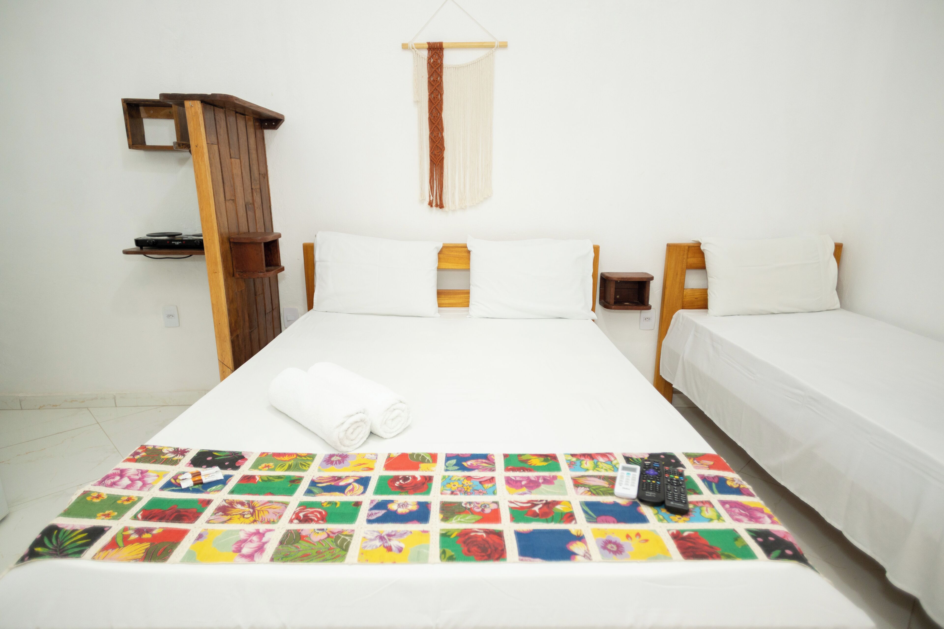 Une chambre d’hôtel avec un lit, deux tables de chevet, une armoire en bois et une couvre-lit à motifs floraux colorés.