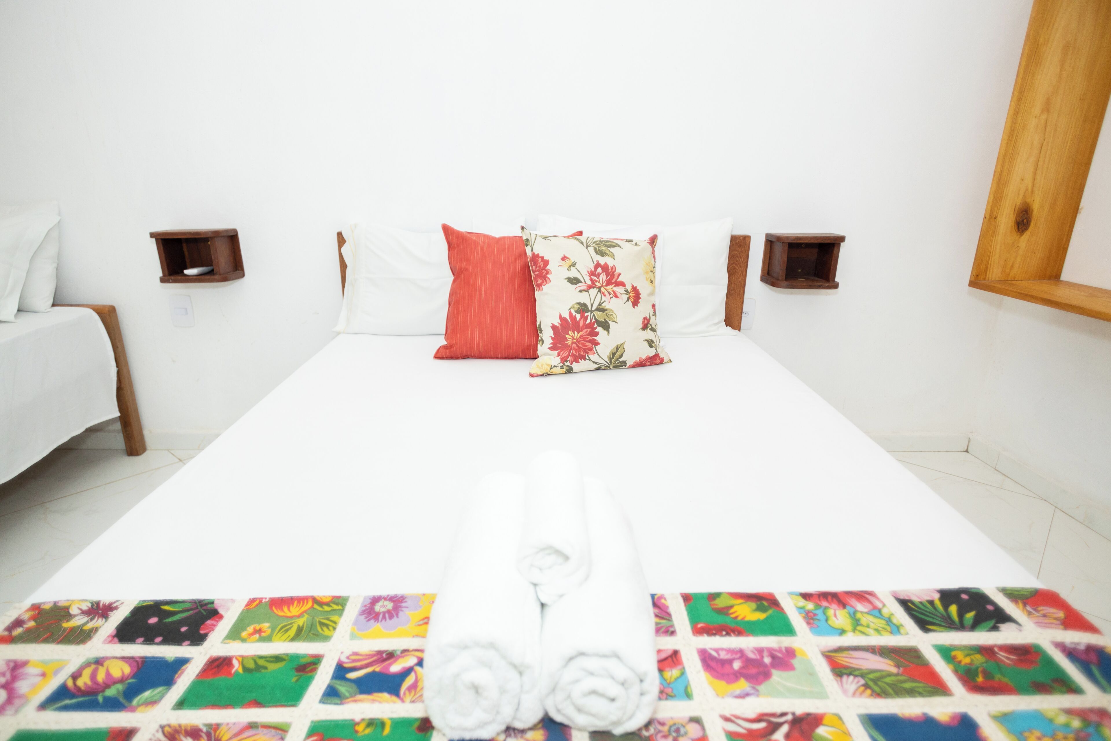 A neatly made bed with white linens, a colorful floral-patterned pillow, and a towel on the bed.