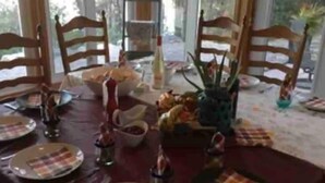 A dining table set for four with a red tablecloth, plates, cutlery, and a centerpiece of fruits and a bottle. - Spacious Waterfront in the French River

 (Noëlville)