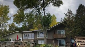A two-story house with a stone foundation, a front porch, and a small deck. - Spacious Waterfront in the French River

 (Noëlville)