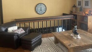 A living room with a wooden bench, a black leather sofa, a wooden coffee table, a chandelier, a wall clock, and a staircase. - Spacious Waterfront in the French River

 (Noëlville)