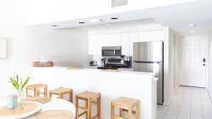 A modern kitchen with white cabinetry, a stainless steel refrigerator, and a central island with stools. - Condo in Vero Beach, Florida  a view of the Marina just outside your Window (Vero Beach)