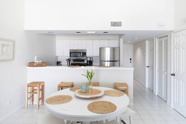 Een moderne keuken met witte kastjes, roestvrijstalen apparatuur en een eethoek met een ronde tafel en krukken.