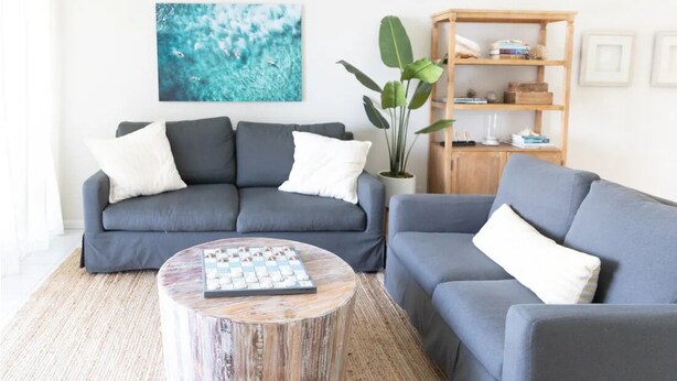 A living room with two grey sofas, a round coffee table, a wooden bookshelf, and a large plant. - Condo in Vero Beach, Florida  a view of the Marina just outside your Window (Vero Beach)