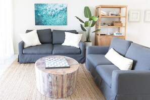 Een woonkamer met twee grijze banken, een ronde salontafel, een houten boekenkast en een grote plant.