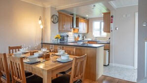 A modern kitchen with wooden cabinets, a central island, and a dining area with a wooden table and chairs. - Isis Lakes 50, Natterjack Lodge - Lakeside Lodge, On-Site Activities, Sleeps 6 (SOUTH CERNEY)