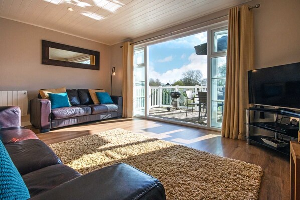 Ein Wohnzimmer mit einer Couch, einem Fernseher und einem großen Fenster mit Blick auf eine Terrasse.