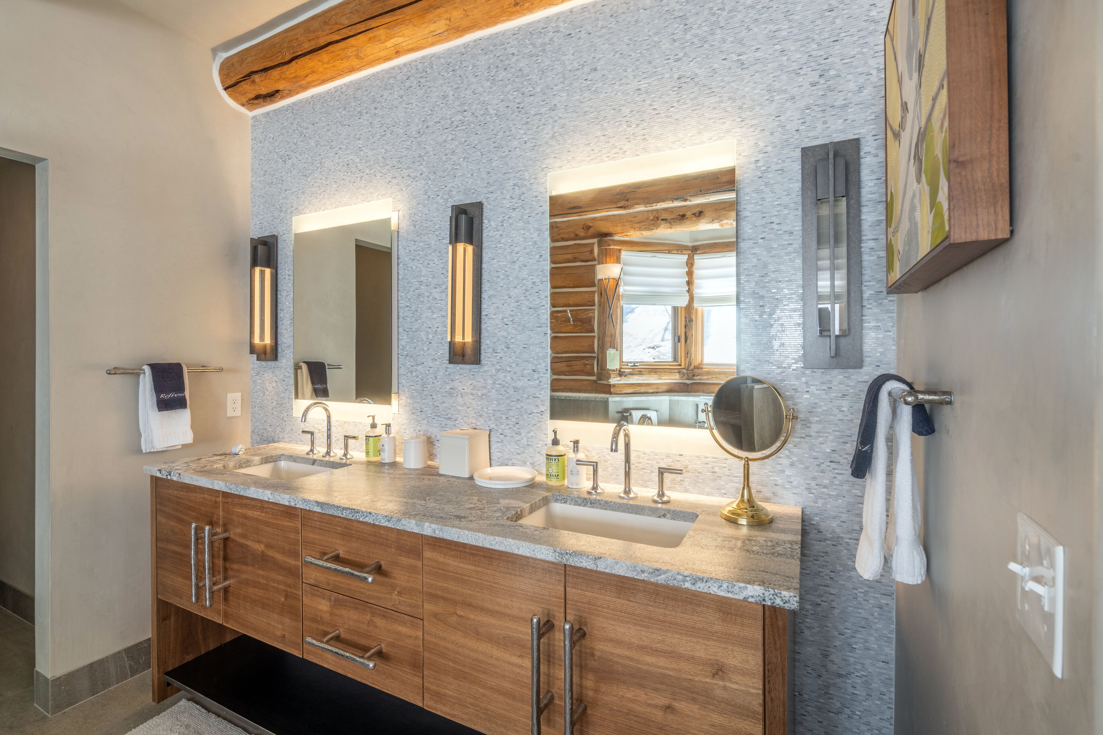 A modern bathroom with a granite countertop, double sinks, wooden cabinets, and a large mirror.