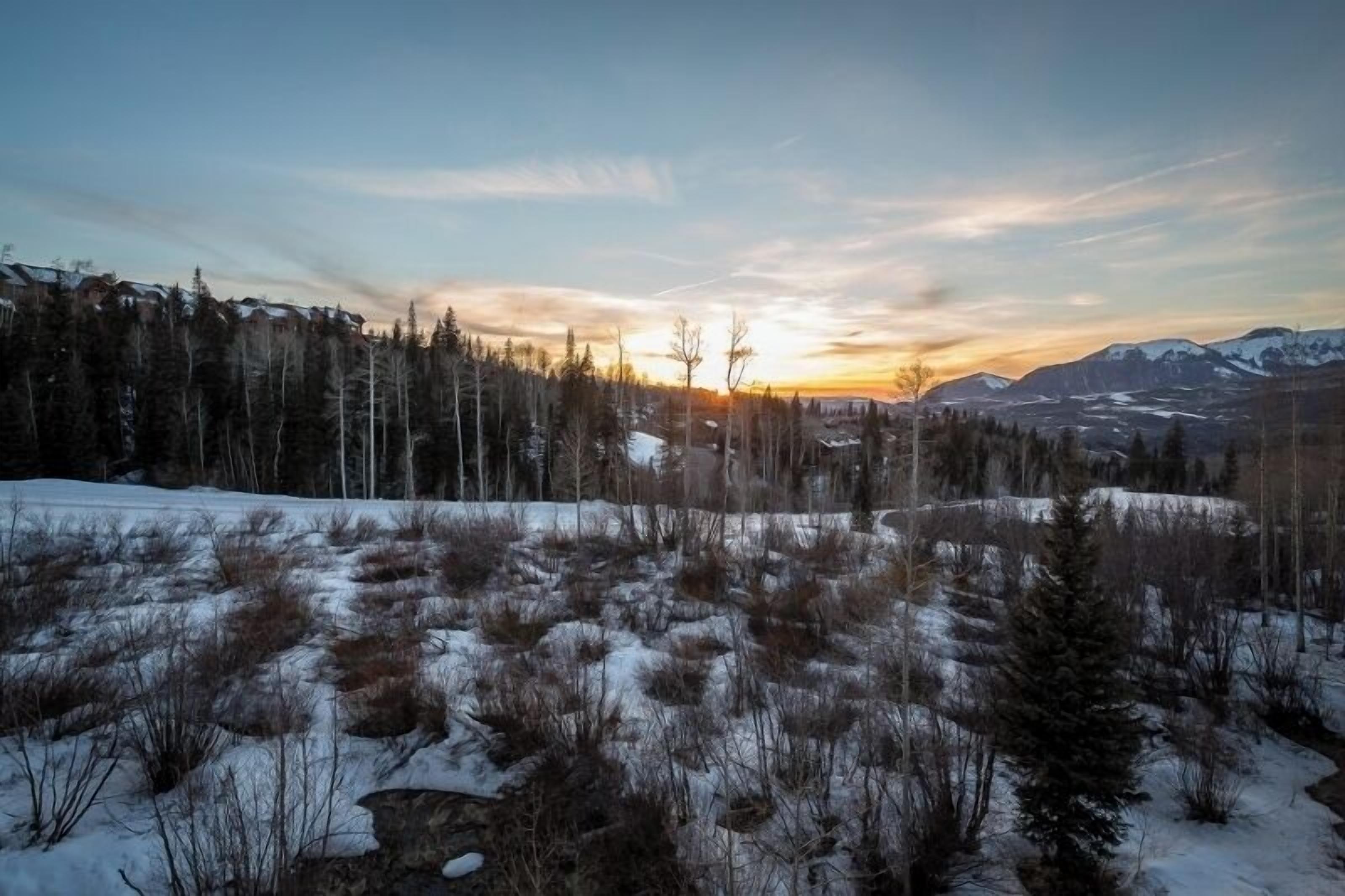 Un paysage montagneux où le sol et les arbres sont recouverts de neige, au coucher du soleil.